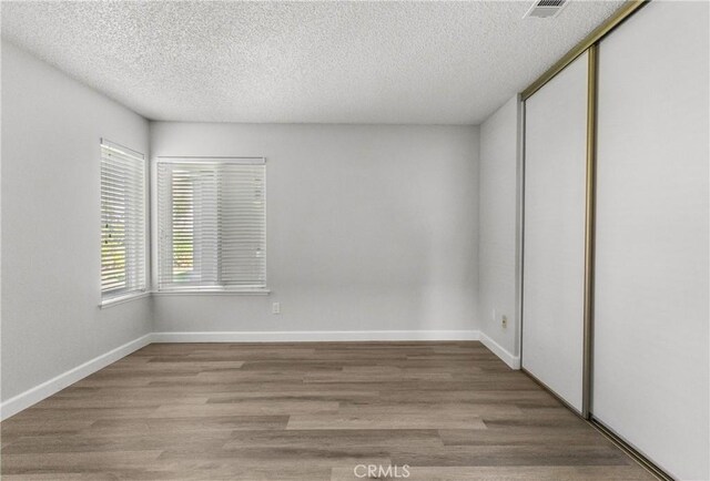 unfurnished room with visible vents, baseboards, a textured ceiling, and wood finished floors