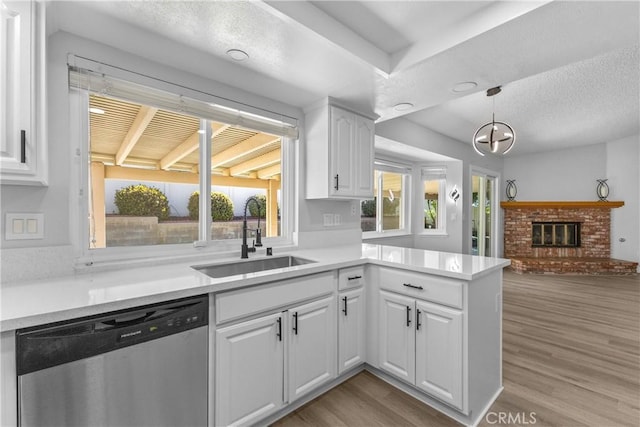 kitchen with dishwasher, a fireplace, a peninsula, wood finished floors, and a sink