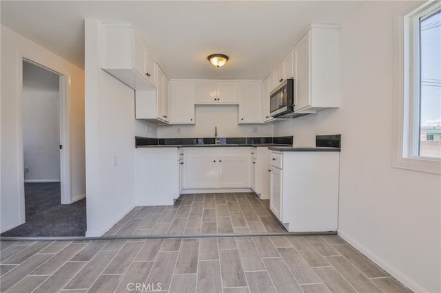 kitchen featuring dark countertops, stainless steel microwave, a sink, and wood finish floors