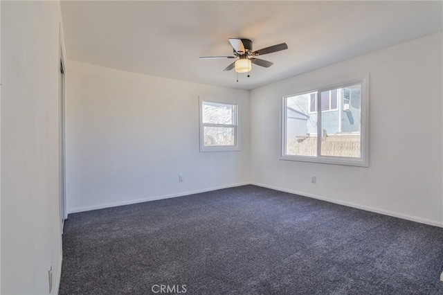 unfurnished room with dark colored carpet, a ceiling fan, and baseboards