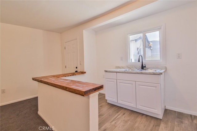 kitchen featuring baseboards, white cabinets, light wood-type flooring, wooden counters, and a sink