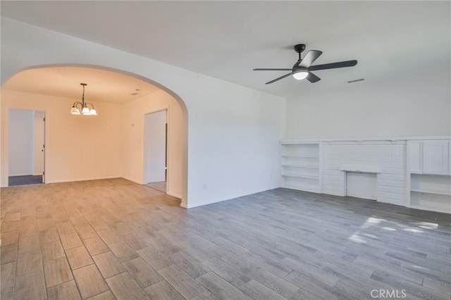 unfurnished living room featuring arched walkways, a fireplace, visible vents, wood finished floors, and ceiling fan with notable chandelier