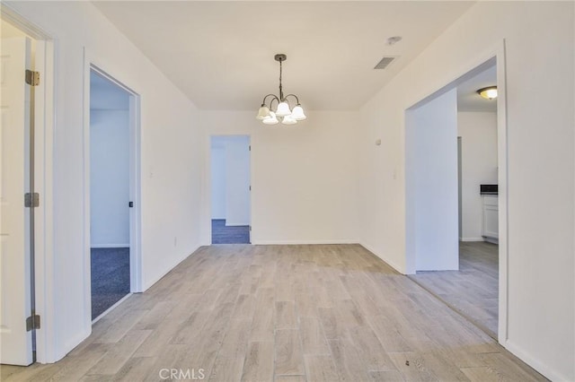 spare room featuring baseboards, light wood-style flooring, visible vents, and an inviting chandelier