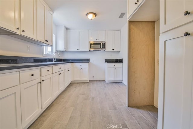 kitchen featuring visible vents, stainless steel microwave, light wood-style flooring, white cabinets, and a sink