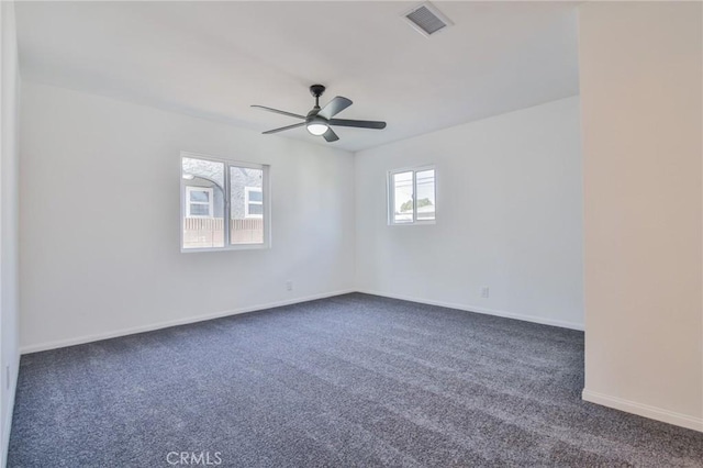 spare room featuring dark colored carpet, a ceiling fan, visible vents, and baseboards