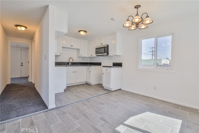 kitchen with dark countertops, white cabinetry, stainless steel microwave, and a sink