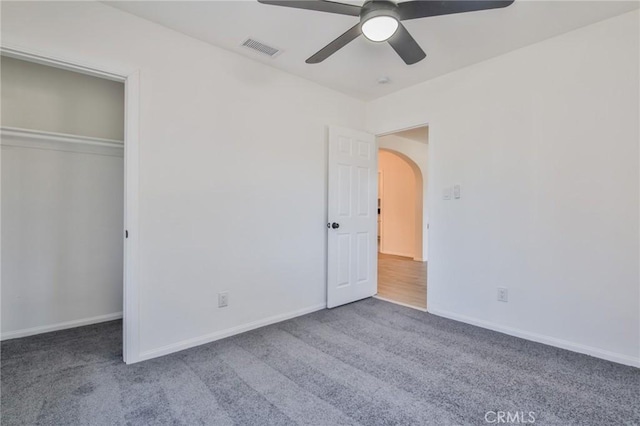 unfurnished bedroom featuring carpet floors, arched walkways, visible vents, and baseboards