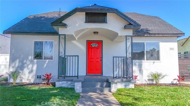 view of front of house with a shingled roof, fence, a front lawn, and stucco siding