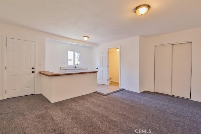 kitchen featuring a peninsula, carpet, baseboards, and a sink