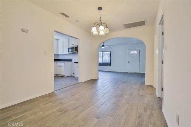 spare room with light wood-style floors, visible vents, and arched walkways