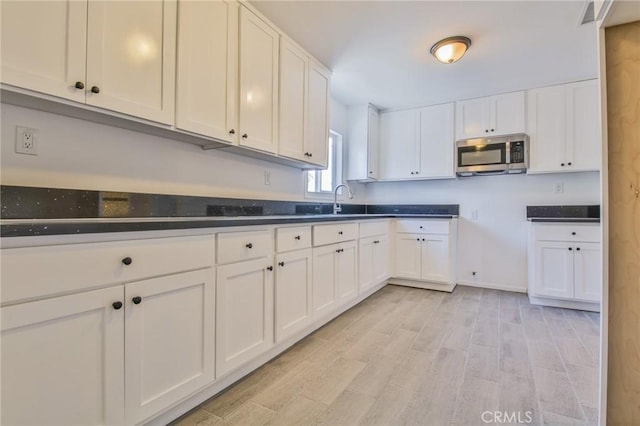 kitchen featuring a sink, white cabinetry, light wood-type flooring, stainless steel microwave, and dark countertops