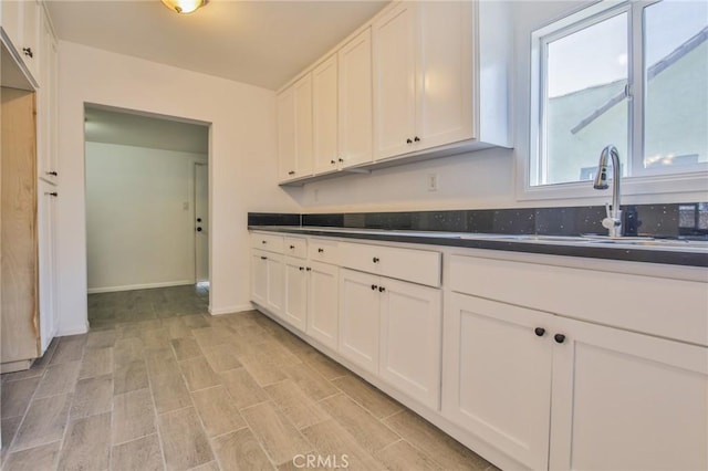 kitchen featuring light wood finished floors, baseboards, white cabinets, dark countertops, and a sink