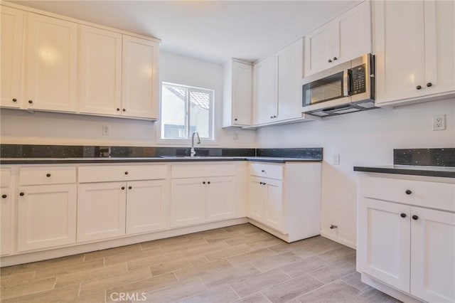 kitchen with dark countertops, wood tiled floor, stainless steel microwave, and a sink