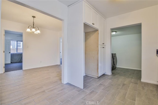 unfurnished room featuring a chandelier, washing machine and clothes dryer, light wood-style flooring, and baseboards