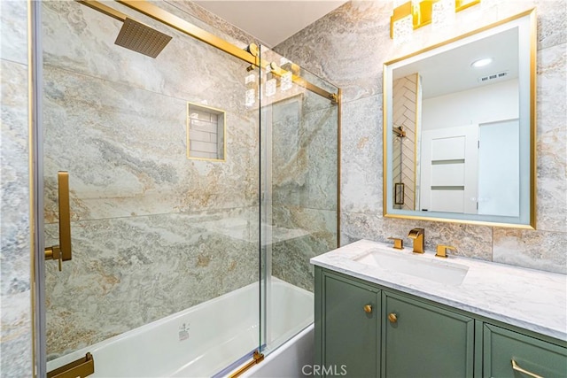 full bathroom featuring shower / bath combination with glass door, vanity, visible vents, and tile walls