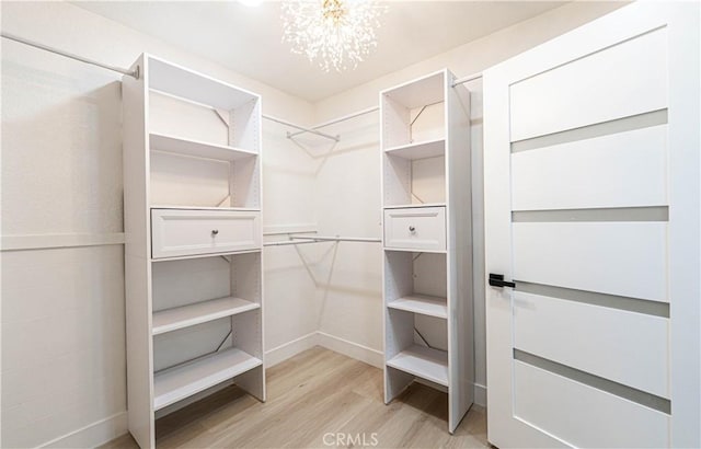 spacious closet with light wood-style floors and a notable chandelier