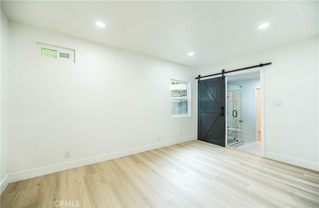 unfurnished bedroom featuring light wood finished floors, a barn door, recessed lighting, and baseboards