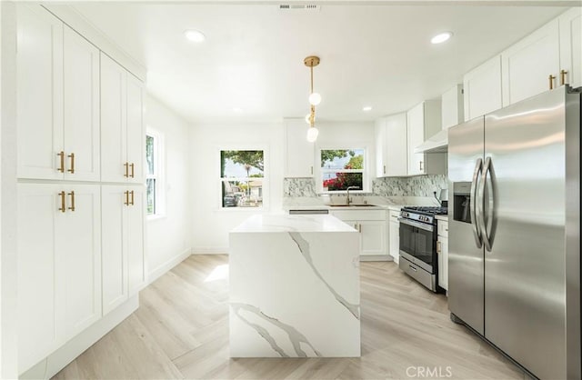 kitchen featuring tasteful backsplash, white cabinets, appliances with stainless steel finishes, light stone counters, and wall chimney range hood