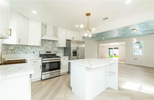 kitchen with a sink, visible vents, white cabinetry, appliances with stainless steel finishes, and wall chimney range hood