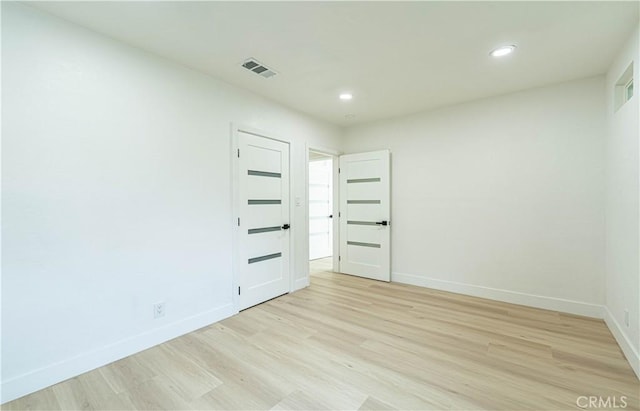 spare room with light wood-style flooring, visible vents, and baseboards