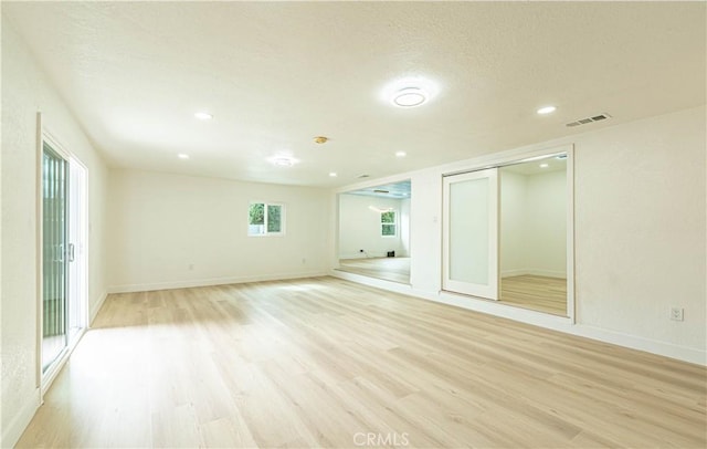 unfurnished room with light wood-style floors, baseboards, visible vents, and a textured ceiling