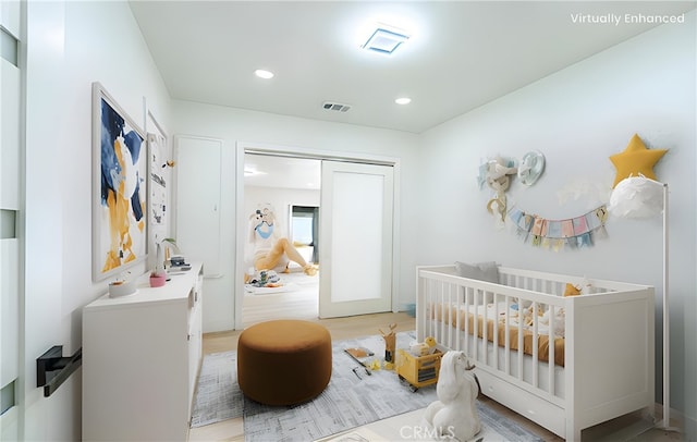 bedroom featuring a crib, light wood finished floors, visible vents, and recessed lighting