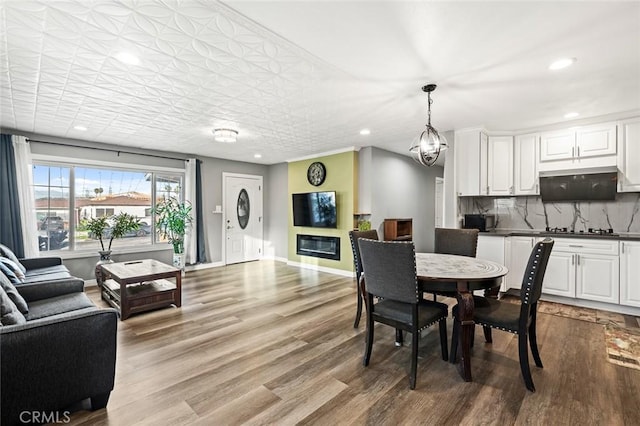 dining room featuring baseboards, a chandelier, recessed lighting, wood finished floors, and a glass covered fireplace