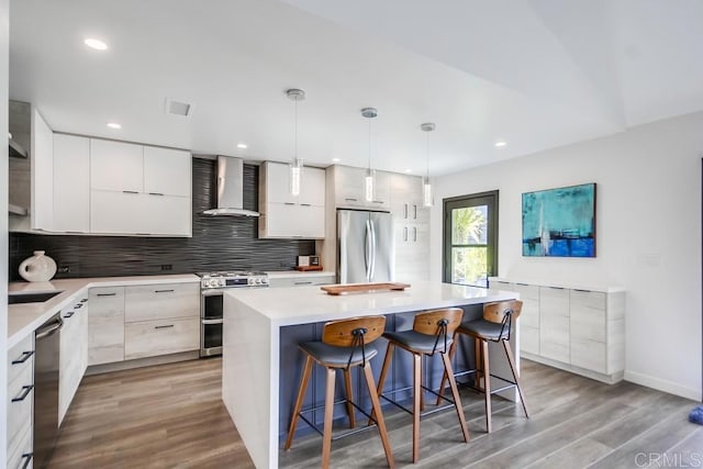 kitchen with a breakfast bar area, stainless steel appliances, wall chimney range hood, modern cabinets, and tasteful backsplash