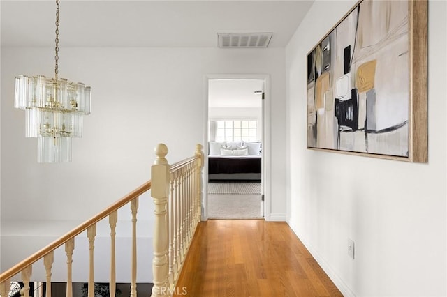 hall with light wood finished floors, visible vents, baseboards, an upstairs landing, and a notable chandelier