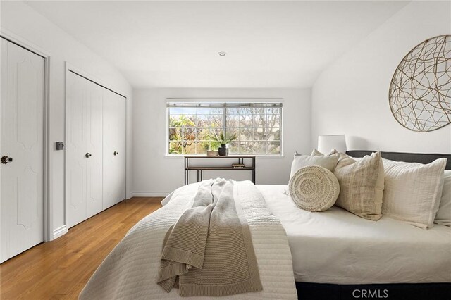 bedroom with multiple closets, lofted ceiling, and wood finished floors