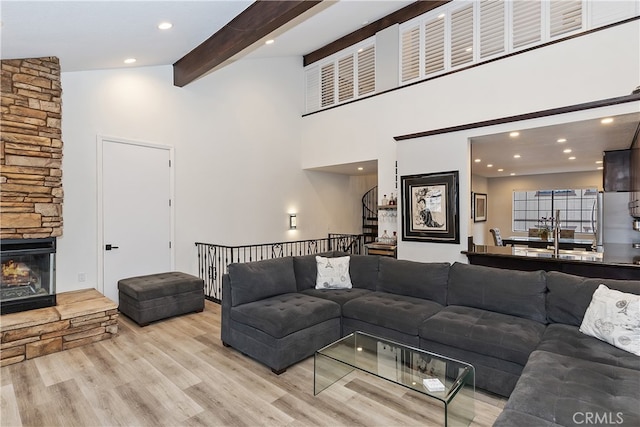 living room with a towering ceiling, stairway, wood finished floors, a stone fireplace, and beam ceiling