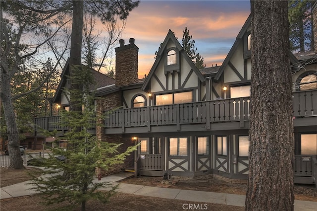 back of property with a balcony, a shingled roof, a chimney, and stucco siding