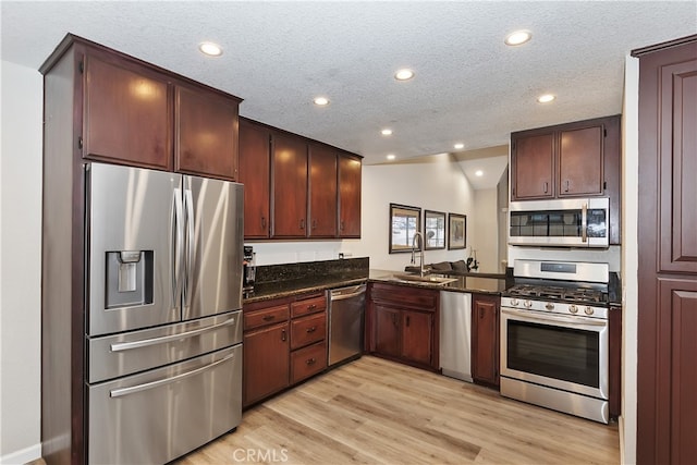 kitchen featuring light wood-style flooring, stainless steel appliances, a textured ceiling, a sink, and recessed lighting