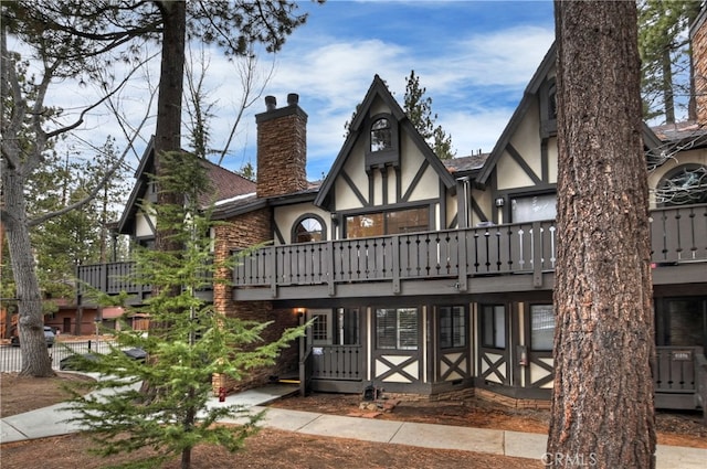 view of front of house featuring a shingled roof, a chimney, a wooden deck, and stucco siding