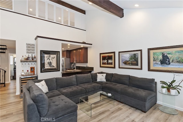 living area with light wood-style floors, beam ceiling, indoor wet bar, and a high ceiling