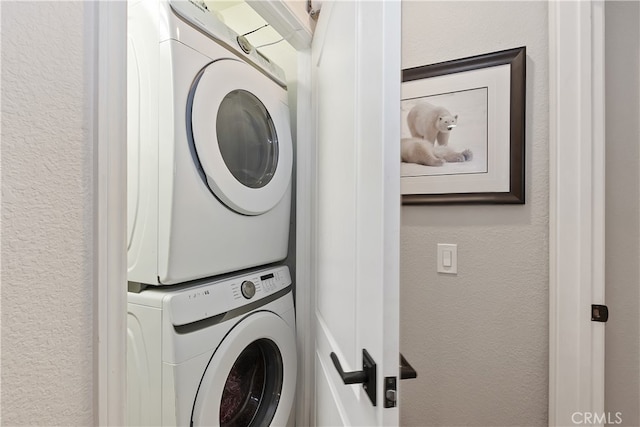 laundry area featuring a textured wall, laundry area, and stacked washer / drying machine