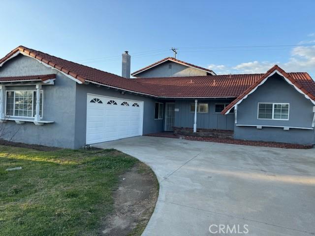 ranch-style home with a tiled roof, concrete driveway, a chimney, and an attached garage