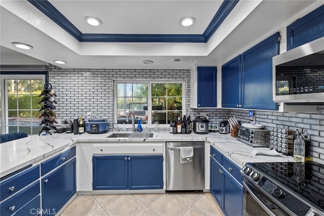 kitchen featuring ornamental molding, blue cabinetry, a tray ceiling, a sink, and stainless steel appliances