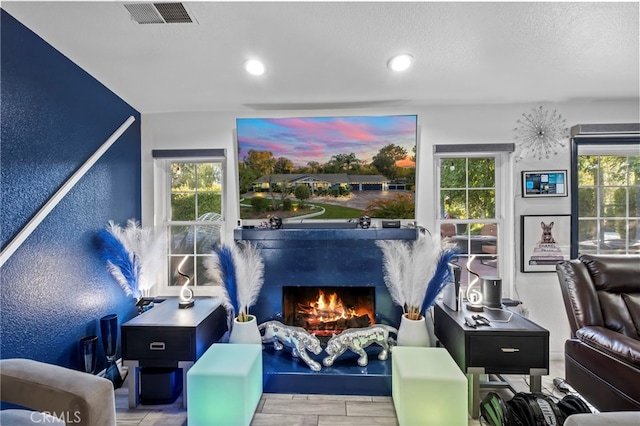 living area featuring visible vents, a warm lit fireplace, a textured ceiling, and a textured wall