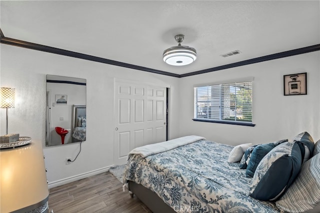 bedroom with crown molding, wood finished floors, visible vents, and baseboards