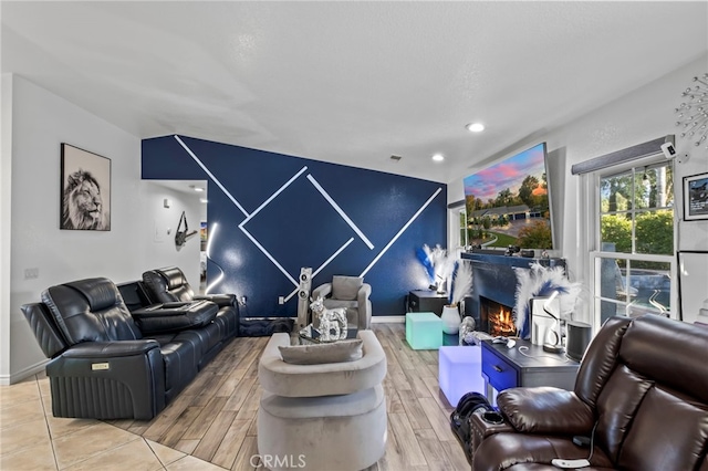 living room with baseboards, wood finish floors, recessed lighting, a warm lit fireplace, and an accent wall