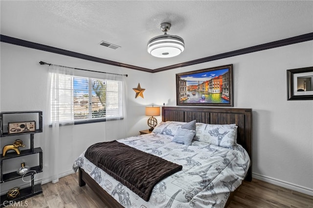 bedroom featuring visible vents, wood finished floors, a textured ceiling, and ornamental molding