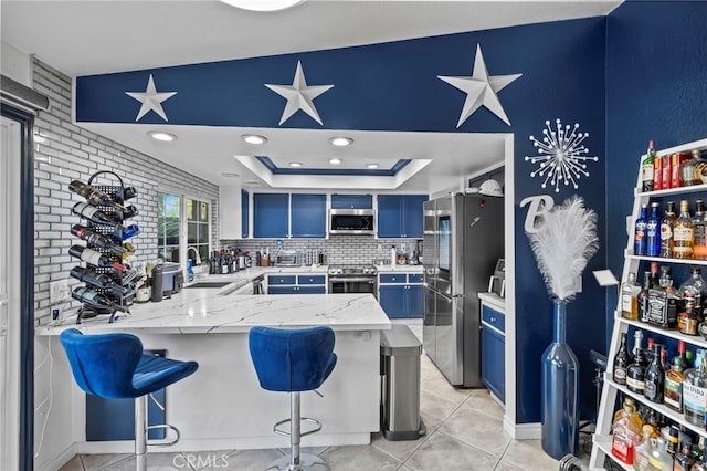 kitchen with a tray ceiling, a peninsula, stainless steel appliances, blue cabinets, and a sink