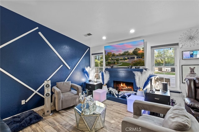 living area with visible vents, wood finished floors, a lit fireplace, recessed lighting, and a textured wall