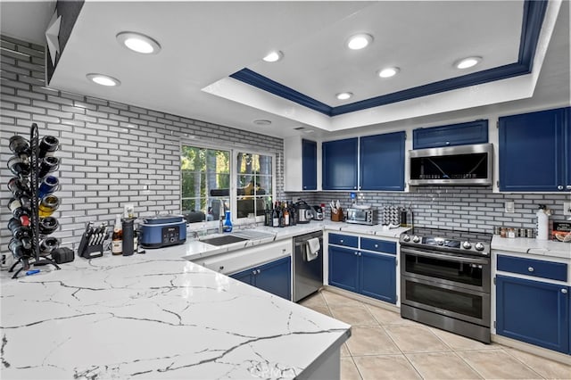 kitchen featuring appliances with stainless steel finishes, a raised ceiling, blue cabinets, and a sink