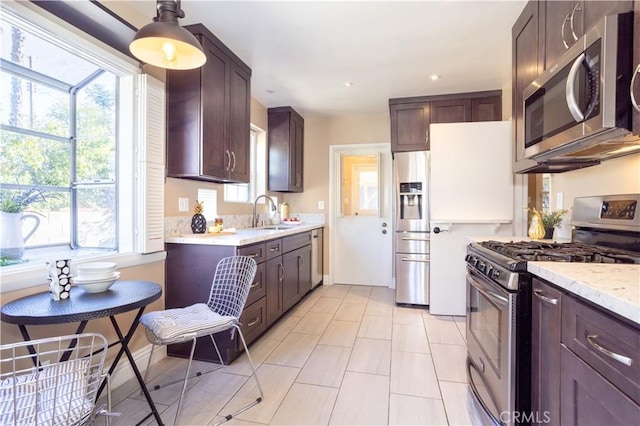 kitchen featuring light stone countertops, stainless steel appliances, dark brown cabinets, a sink, and recessed lighting