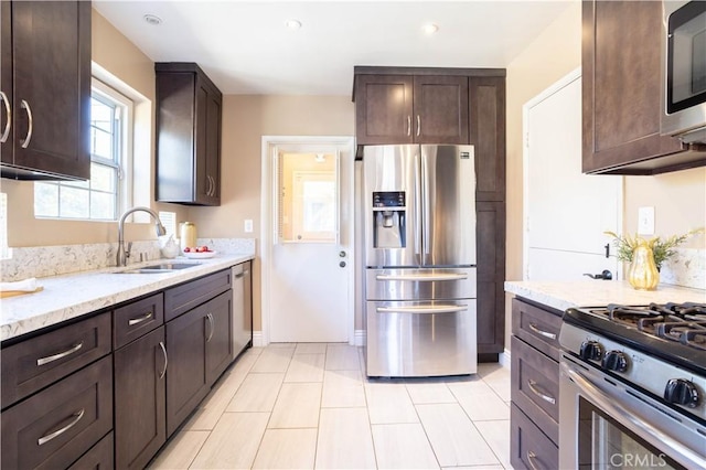 kitchen featuring stainless steel appliances, a sink, dark brown cabinetry, and light stone countertops