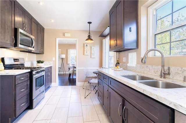 kitchen featuring light stone counters, pendant lighting, stainless steel appliances, a sink, and dark brown cabinetry