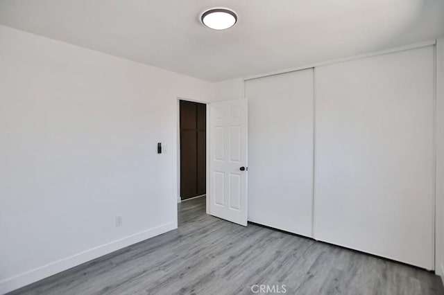 unfurnished bedroom with wood finished floors, baseboards, and a closet