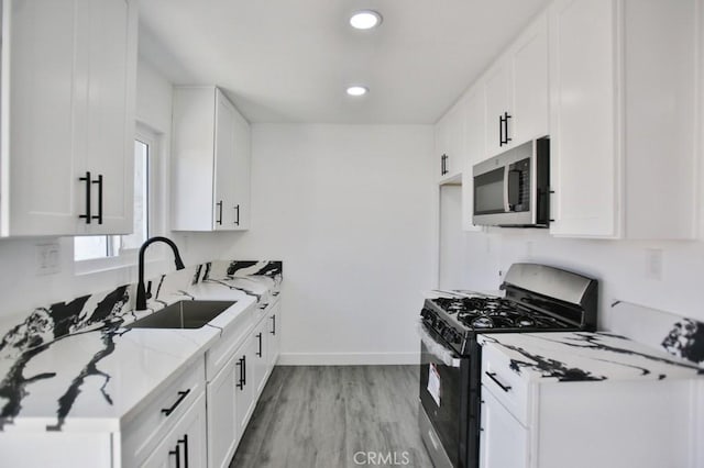 kitchen with a sink, white cabinets, light stone counters, and stainless steel appliances